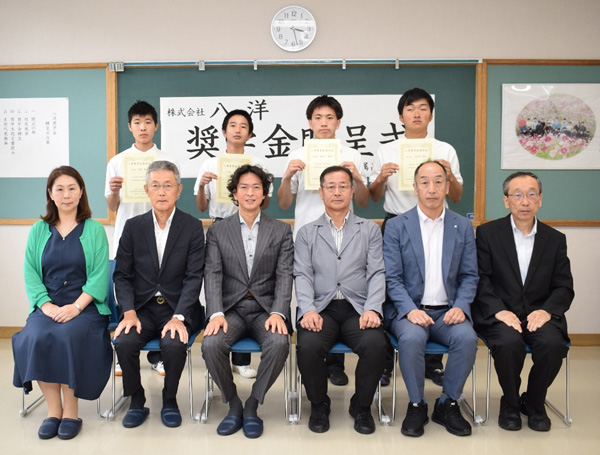 奨学生認定書を手にする生徒4名（後列）と平野校長（前列中央右）、後藤副社長（中央左）